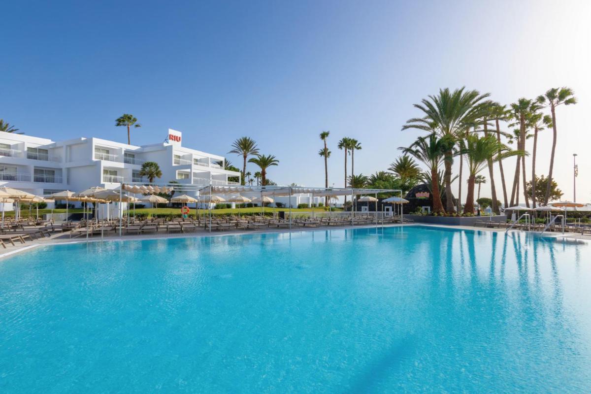 Una gran piscina con sillas y palmeras. en Hotel Riu Paraiso Lanzarote - All Inclusive, en Puerto del Carmen