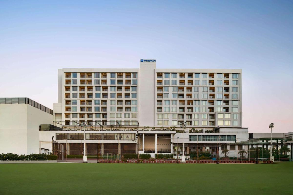 a large building with a green field in front of it at Wyndham Ahmedabad Shela in Ahmedabad