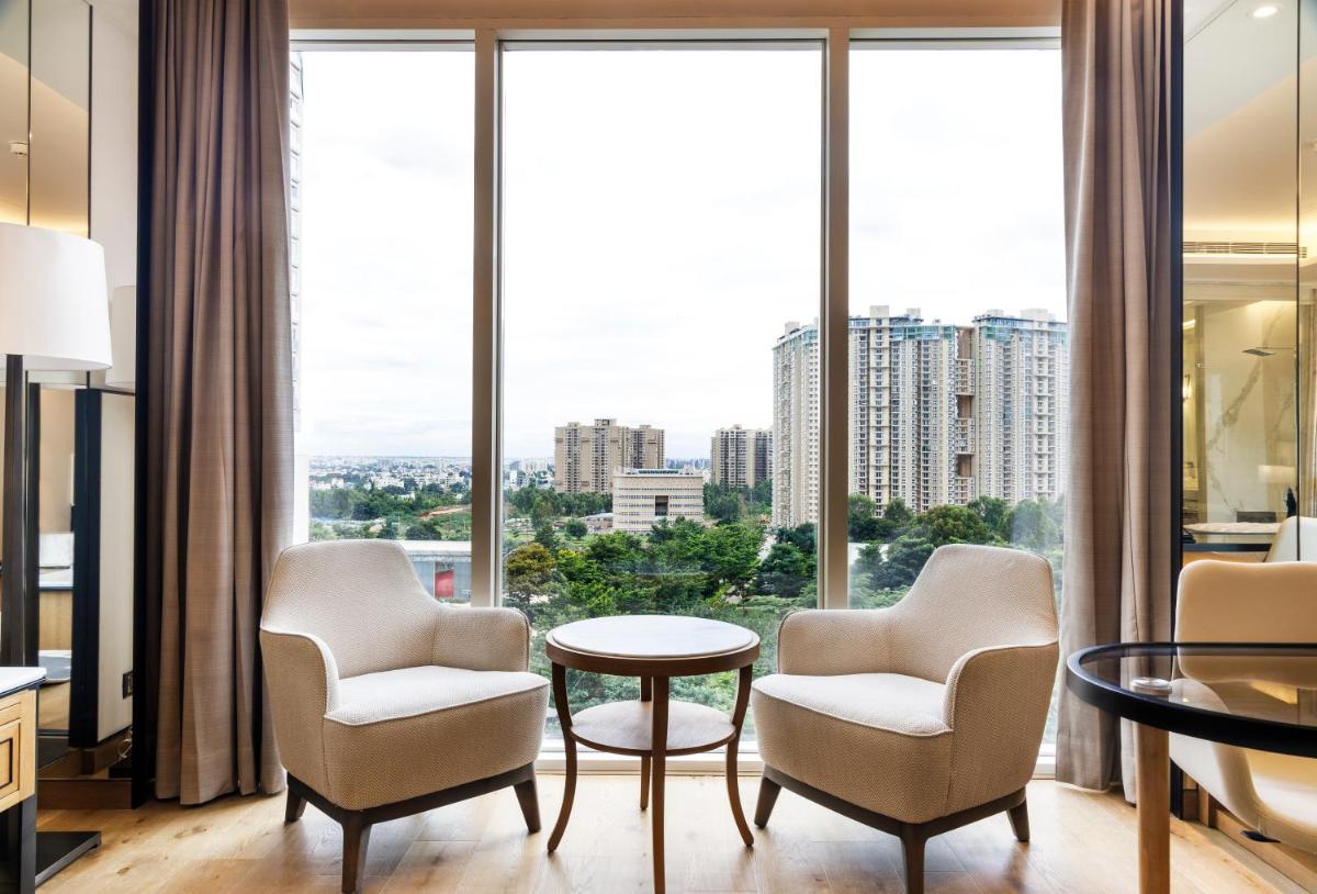a living room with two chairs and a table and large windows at The Leela Bhartiya City Bengaluru in Bengaluru a living room with two chairs and a table and large windows at The Leela Bhartiya City Bengaluru in Bengaluru