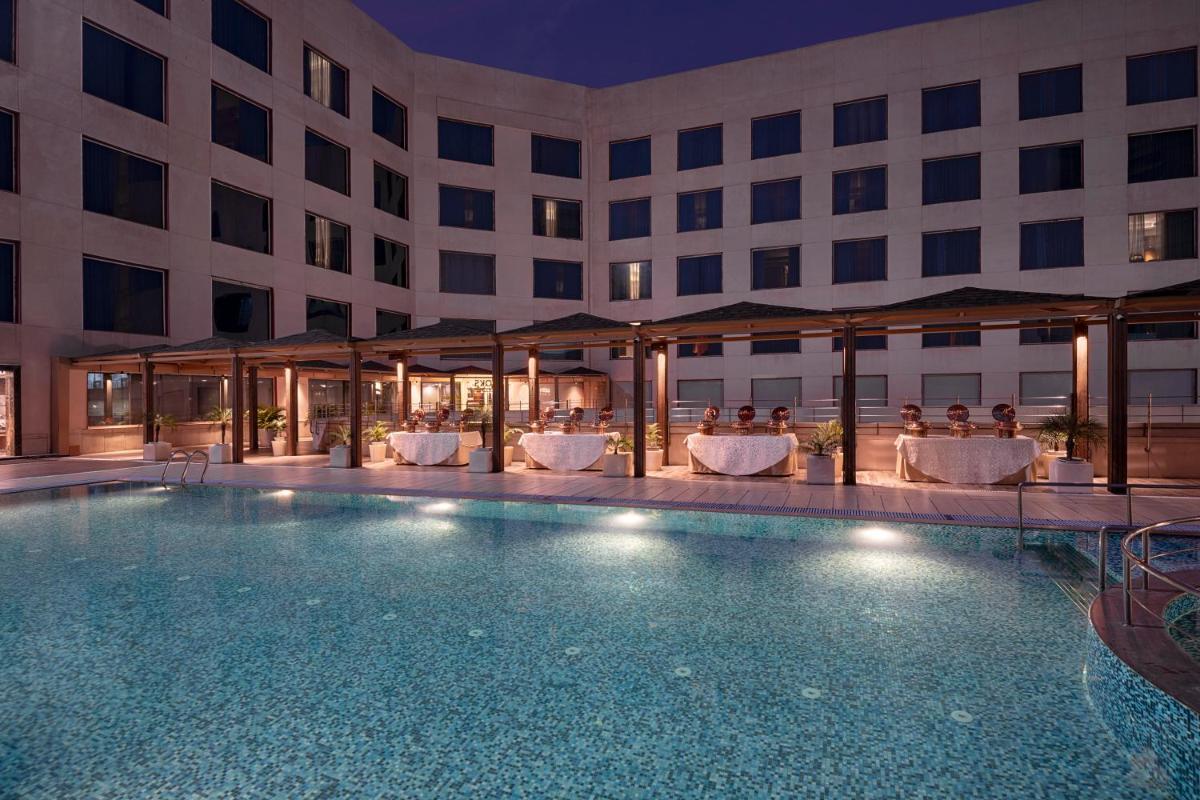 a hotel swimming pool with people sitting in chairs at Radisson Blu Kaushambi Delhi NCR in Ghaziabad