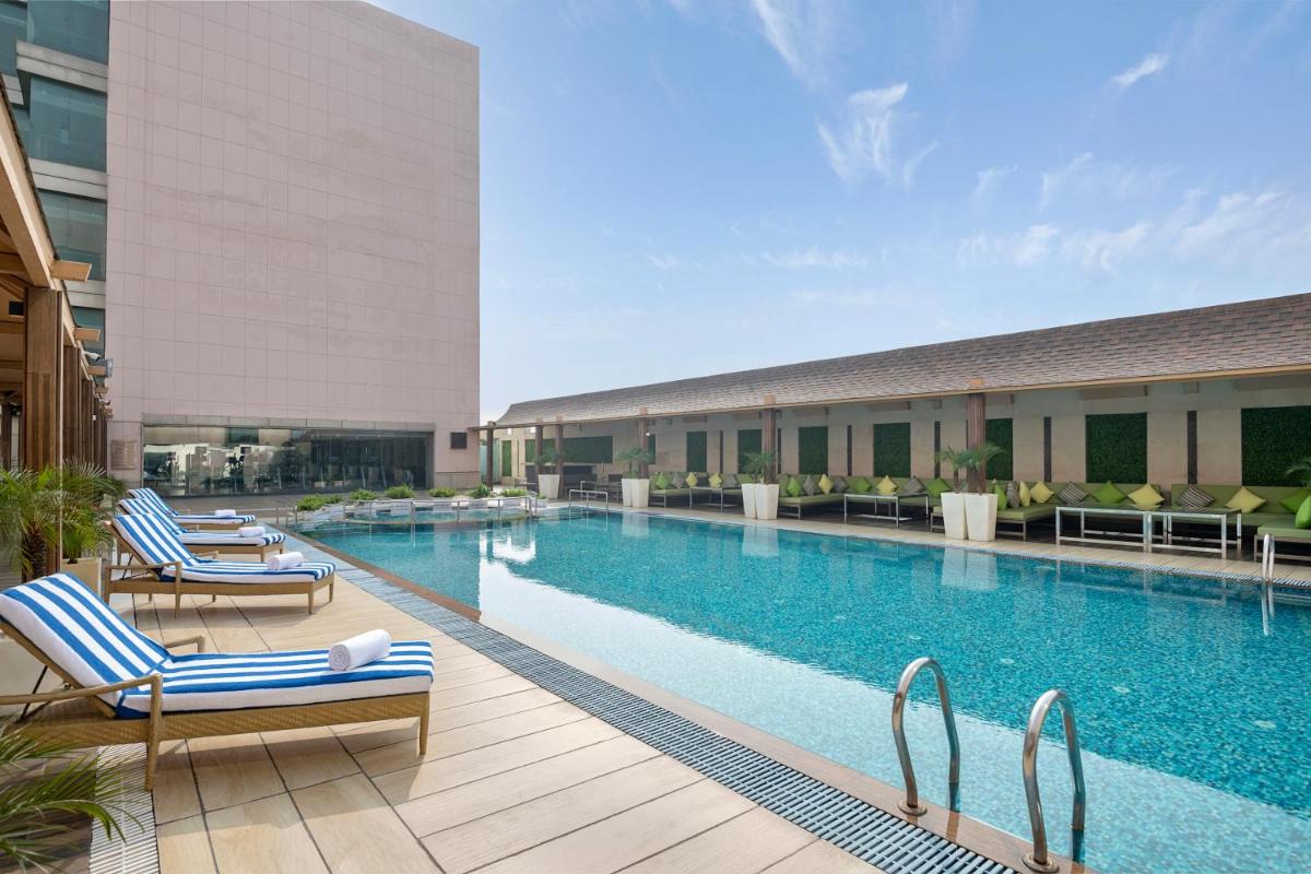 a swimming pool with two lounge chairs and a building at Radisson Blu Kaushambi Delhi NCR in Ghaziabad