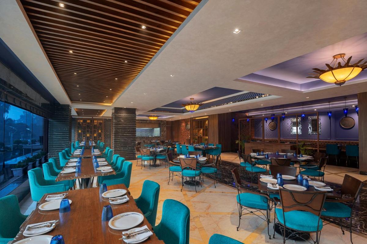 a restaurant with wooden tables and blue chairs at Radisson Blu Kaushambi Delhi NCR in Ghaziabad