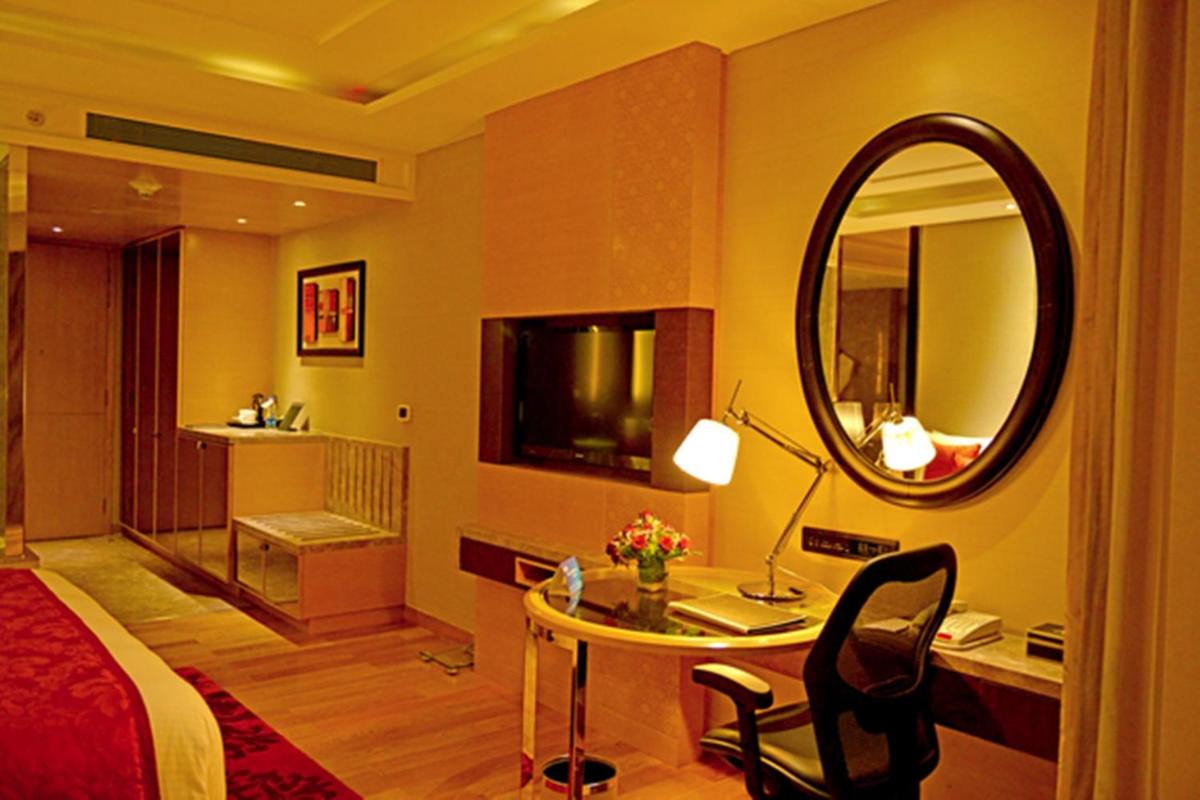 a bedroom with a bed and a desk with a mirror at Radisson Blu Jaipur in Jaipur