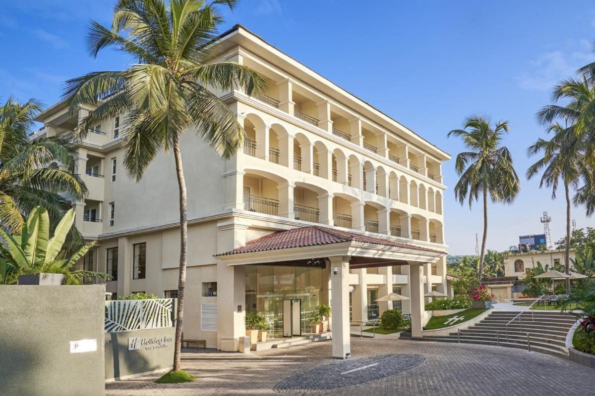 a large white building with palm trees in front of it at Holiday Inn Goa Candolim in Candolim a large white building with palm trees in front of it at Holiday Inn Goa Candolim in Candolim