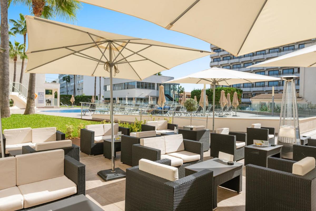 Un patio con sillas y sombrillas y una piscina. en Trendhotel Alcudia - Adults Only, en Puerto de Alcudia