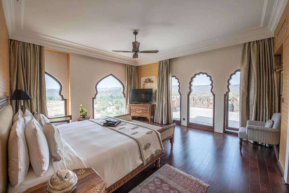 a bedroom with a bed and a tv and windows at Fairmont Jaipur in Jaipur