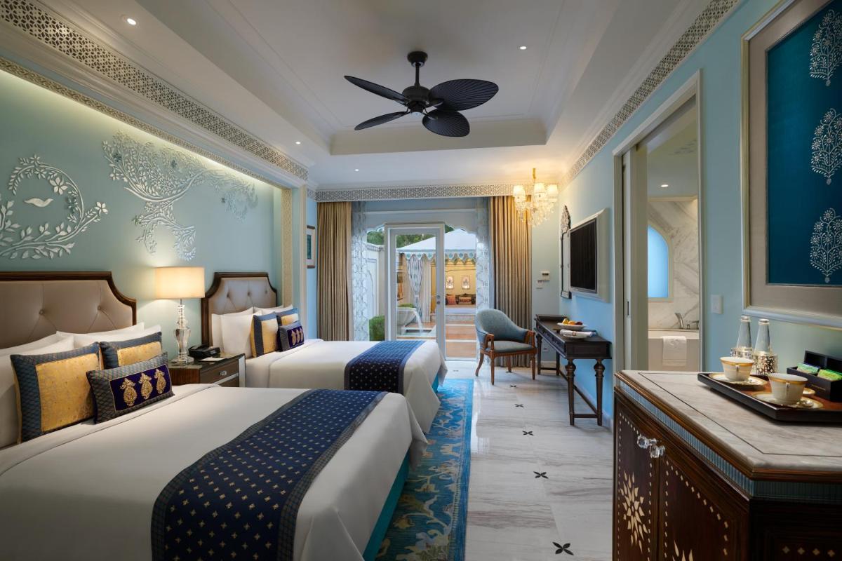 a hotel room with two beds and a desk and a bathroom at The Leela Palace Jaipur in Jaipur