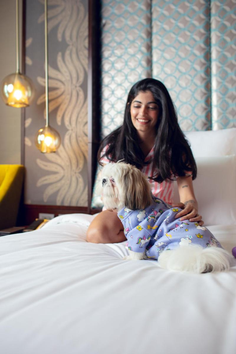 a woman sitting on a bed with a small dog at Pullman New Delhi Aerocity in New Delhi a woman sitting on a bed with a small dog at Pullman New Delhi Aerocity in New Delhi