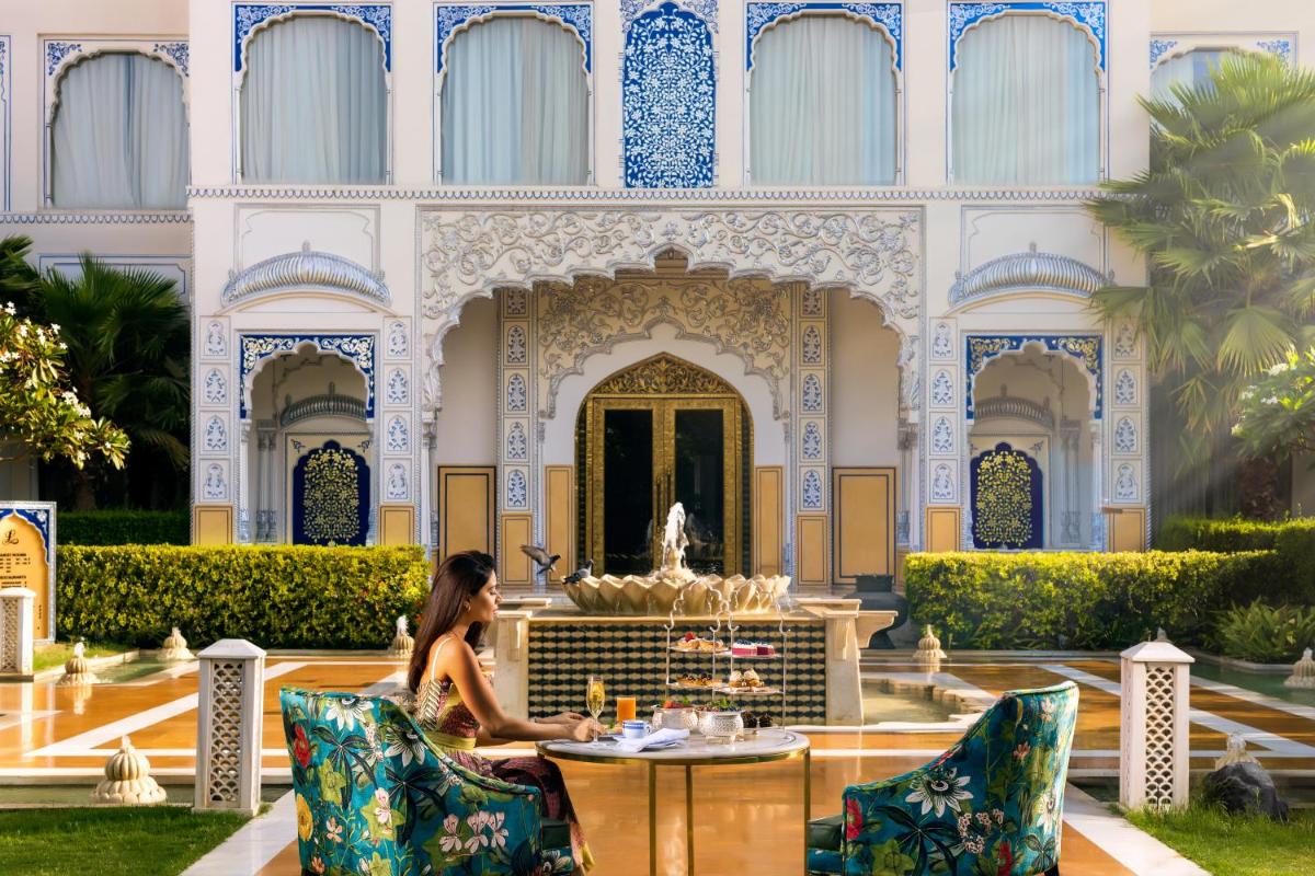a woman sitting in front of a building with a fountain at The Leela Palace Jaipur in Jaipur