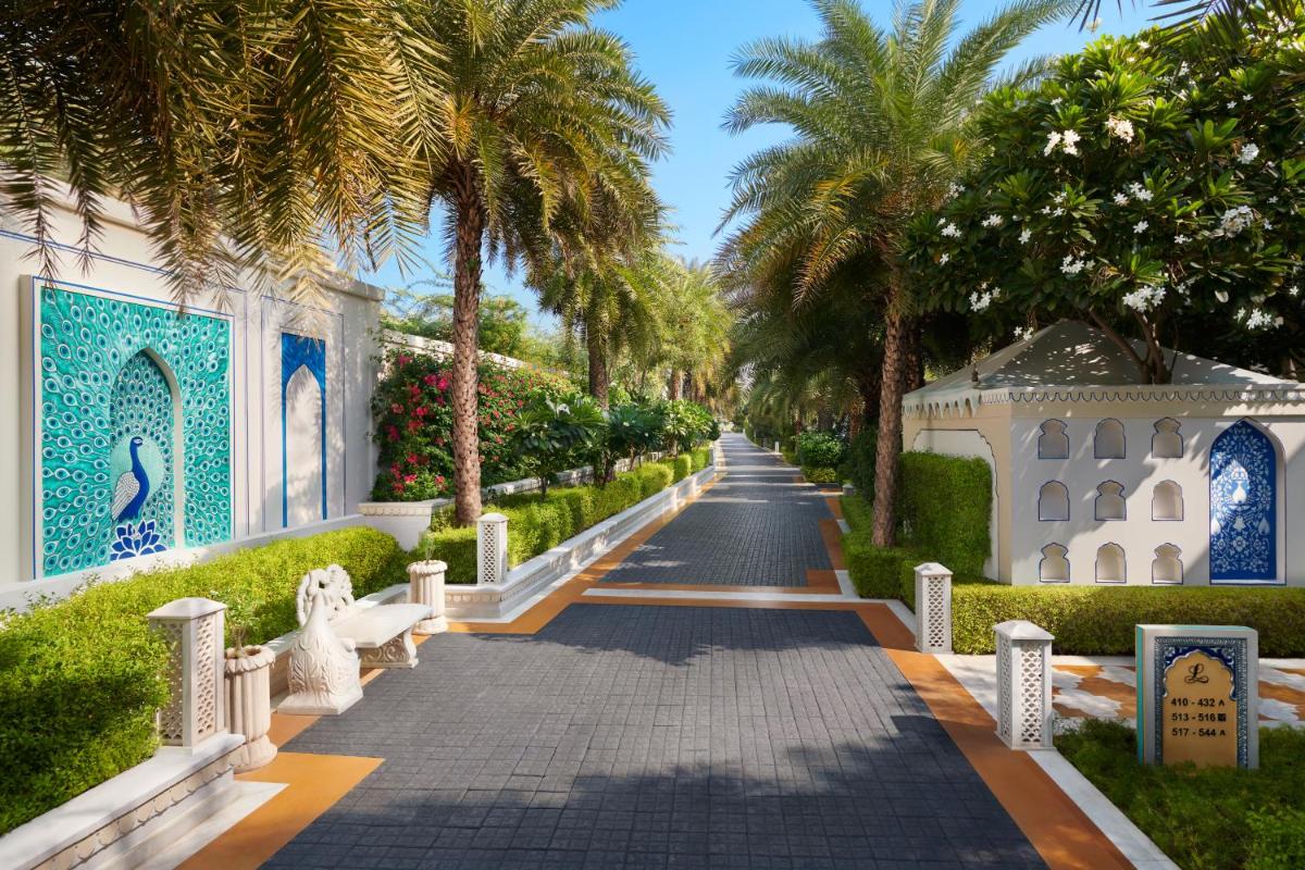 a walkway with palm trees and a building at The Leela Palace Jaipur in Jaipur