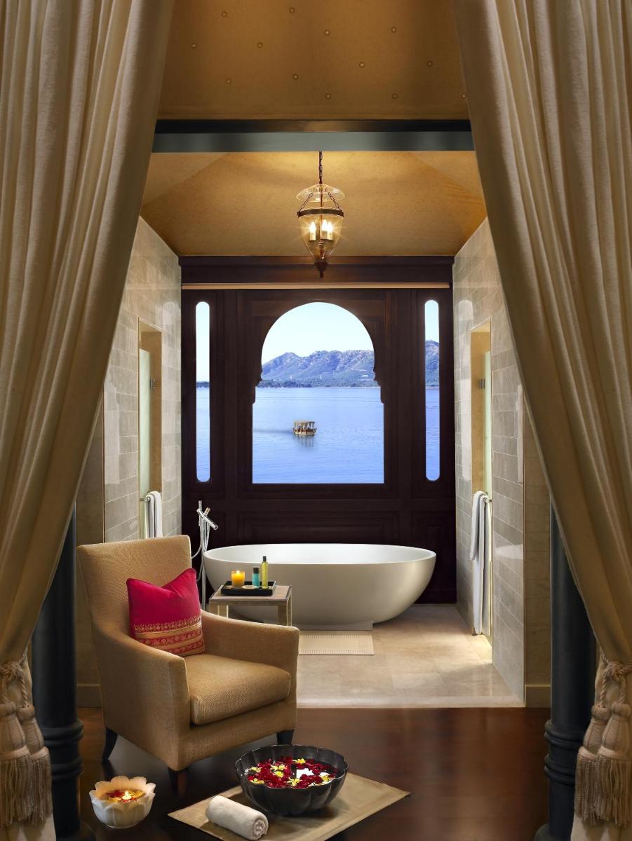 a bathroom with a tub and a chair and a window at The Leela Palace Udaipur in Udaipur a bathroom with a tub and a chair and a window at The Leela Palace Udaipur in Udaipur