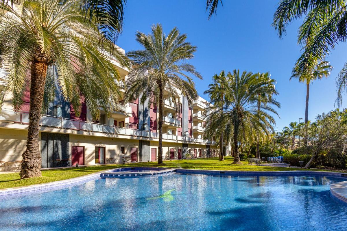 Una piscina con palmeras frente a un edificio. en Daniya Denia Spa & Business 4*, en Denia