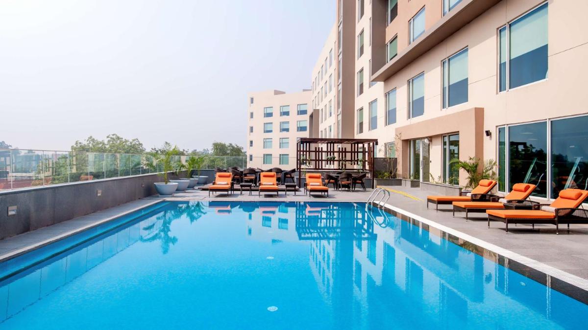 a swimming pool with lounge chairs and a building at Hyatt Place Gurgaon Udyog Vihar in Gurgaon