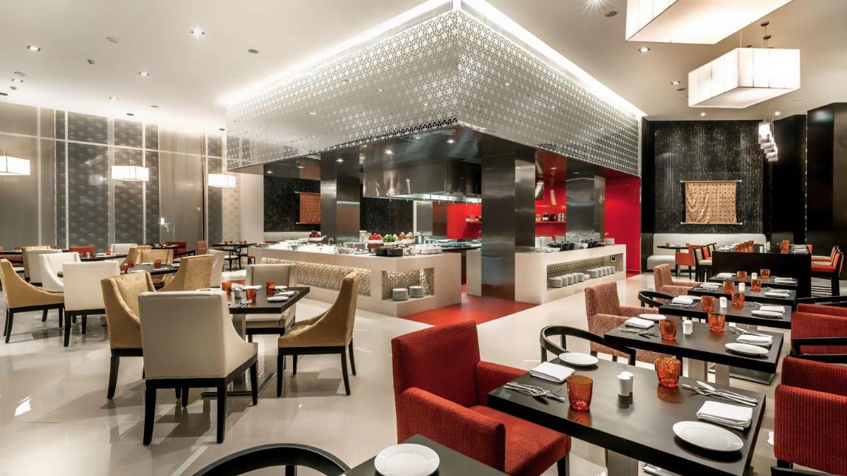 a restaurant with tables and chairs and a kitchen at Hyatt Place Gurgaon Udyog Vihar in Gurgaon