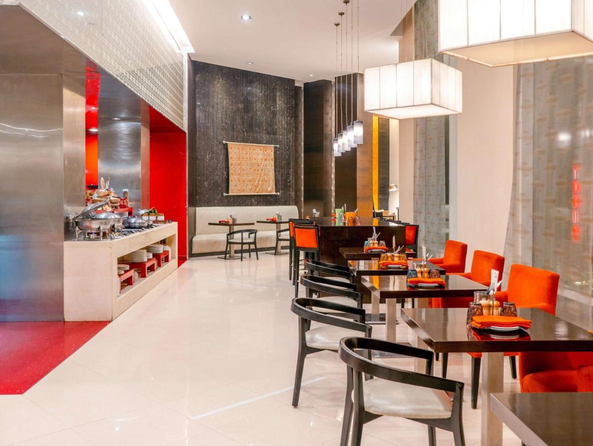 a restaurant with tables and chairs and a kitchen at Hyatt Place Gurgaon Udyog Vihar in Gurgaon