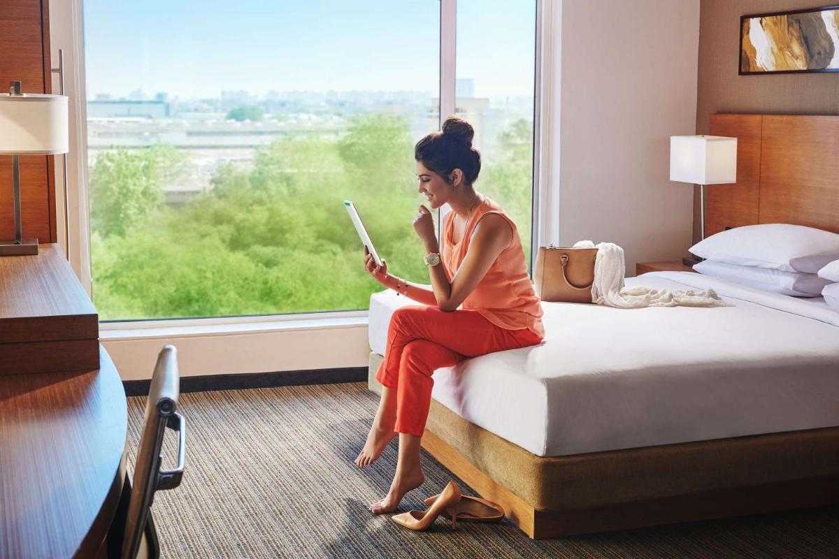 a woman sitting on a bed looking at her tablet at Hyatt Place Gurgaon Udyog Vihar in Gurgaon