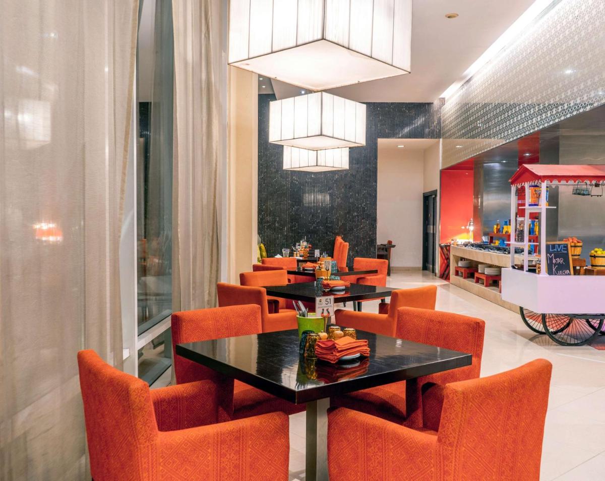 a restaurant with orange chairs and a black table at Hyatt Place Gurgaon Udyog Vihar in Gurgaon
