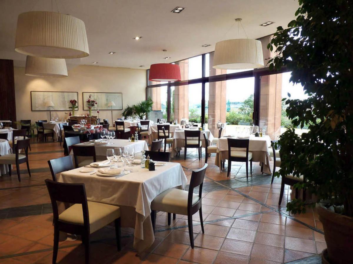 Un restaurante con mesas y sillas blancas y grandes ventanales. en Hotel Cigarral el Bosque, en Toledo