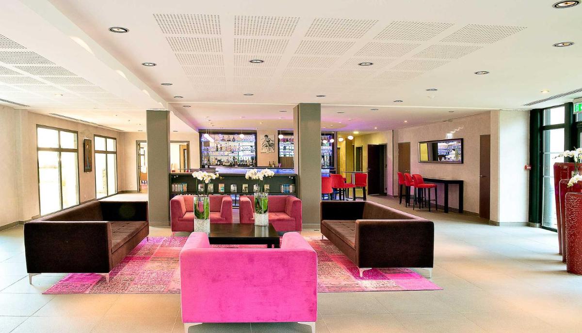 un hall avec des meubles roses et un bar en arrière-plan dans l'établissement Thalasso Concarneau Spa Marin Resort, à Concarneau