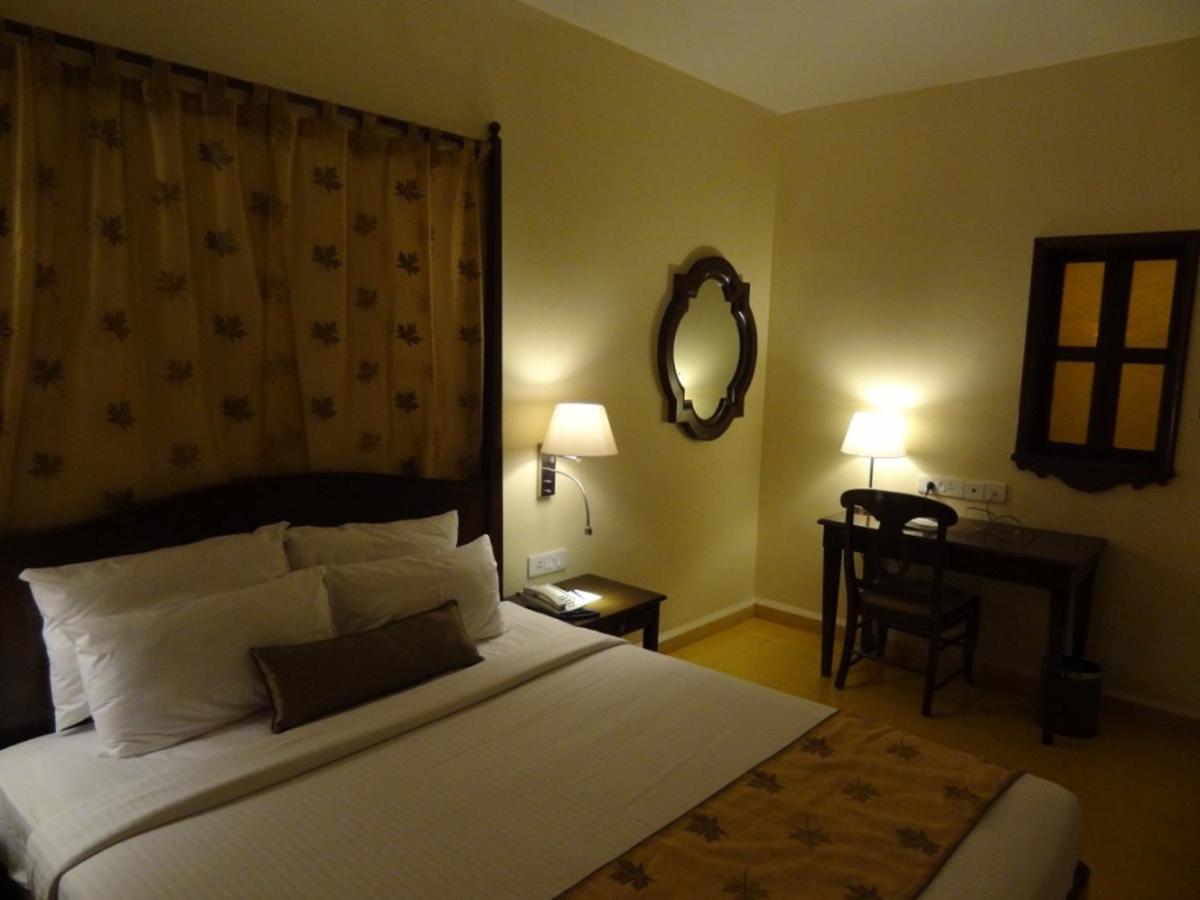 a bedroom with a bed and a table and a mirror at The Crown Goa in Panaji