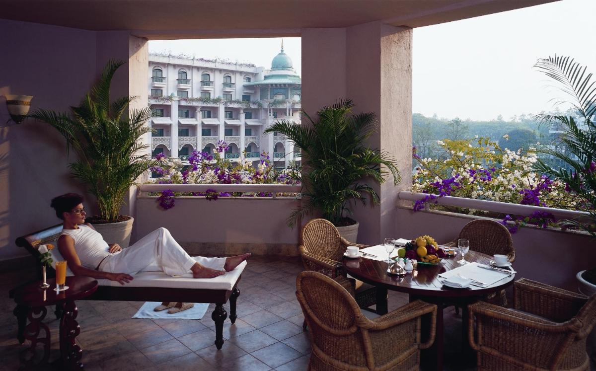 a woman sitting in a chair on a balcony with a table at The Leela Palace Bengaluru in Bengaluru a woman sitting in a chair on a balcony with a table at The Leela Palace Bengaluru in Bengaluru
