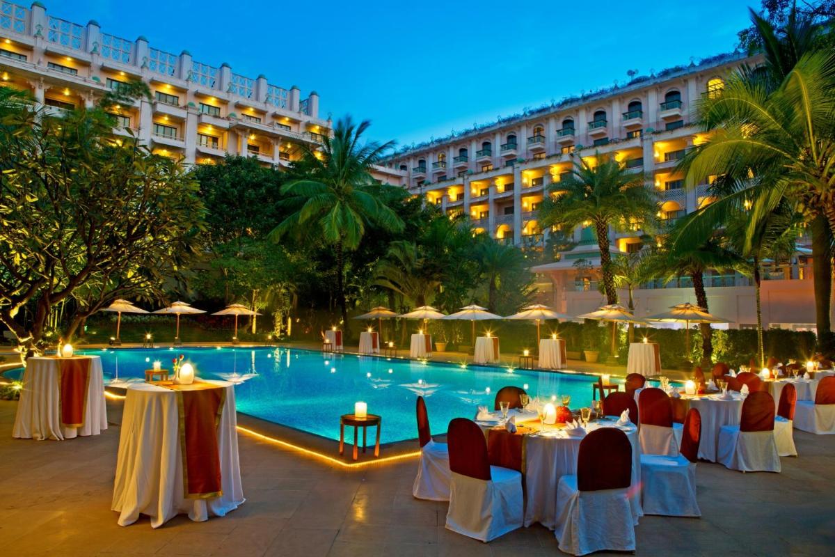 a hotel patio with tables and a pool at night at The Leela Palace Bengaluru in Bengaluru a hotel patio with tables and a pool at night at The Leela Palace Bengaluru in Bengaluru