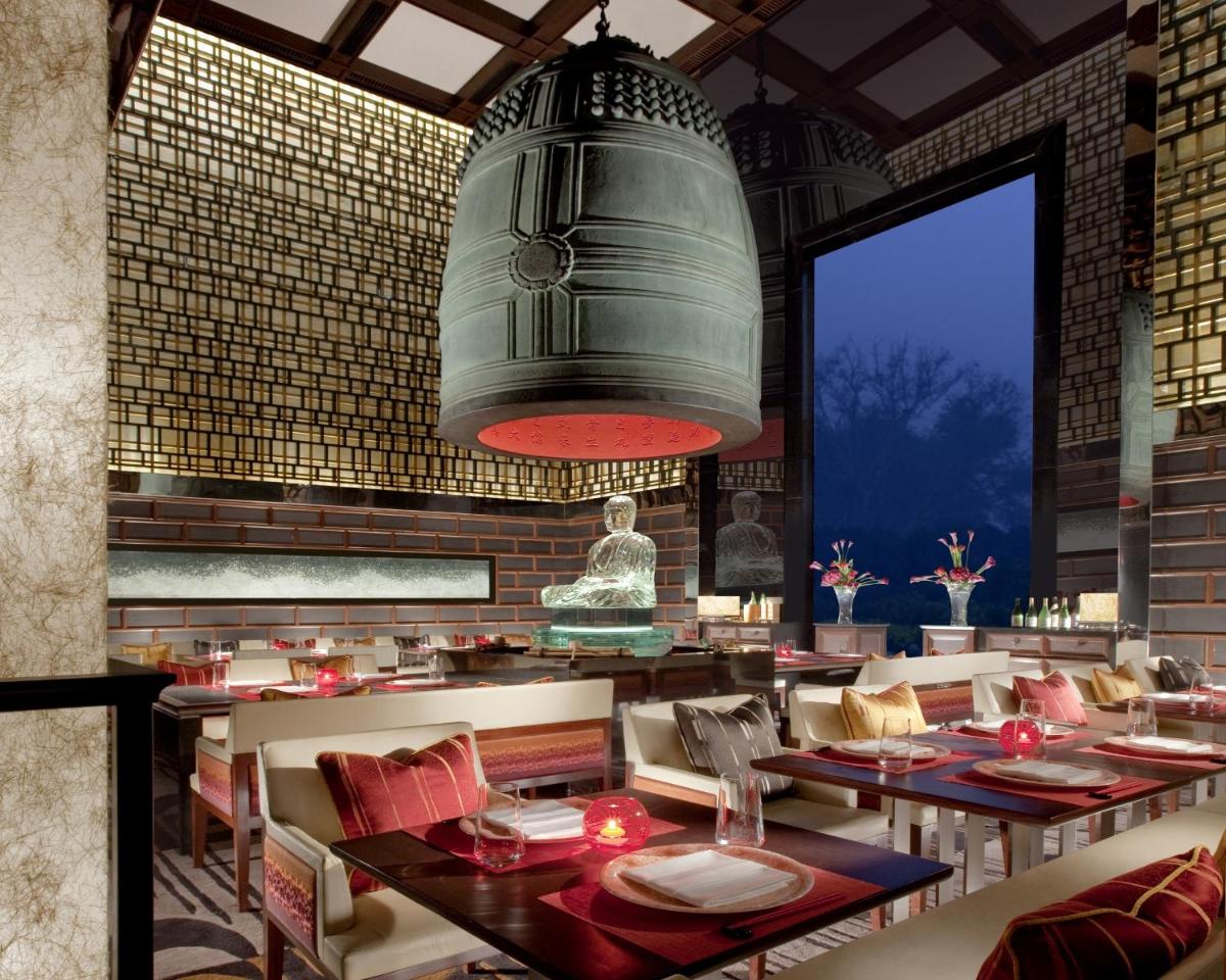 a restaurant with tables and chairs and a large light fixture at The Leela Palace New Delhi in New Delhi a restaurant with tables and chairs and a large light fixture at The Leela Palace New Delhi in New Delhi