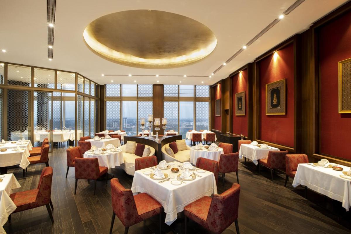 a restaurant with white tables and chairs and windows at The Leela Bhartiya City Bengaluru in Bengaluru a restaurant with white tables and chairs and windows at The Leela Bhartiya City Bengaluru in Bengaluru