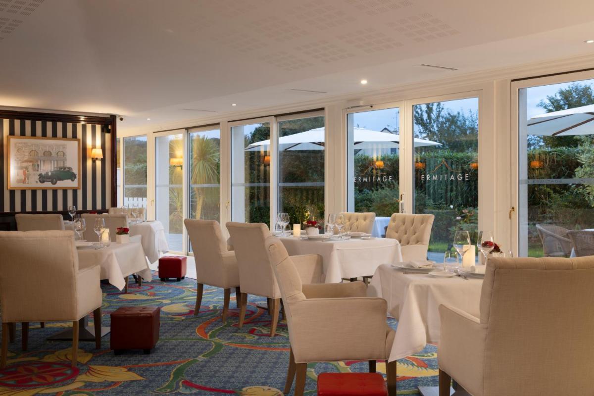 un restaurant avec des tables et des chaises blanches et des fenêtres dans l'établissement Ermitage - Mont-Saint-Michel, à Beauvoir