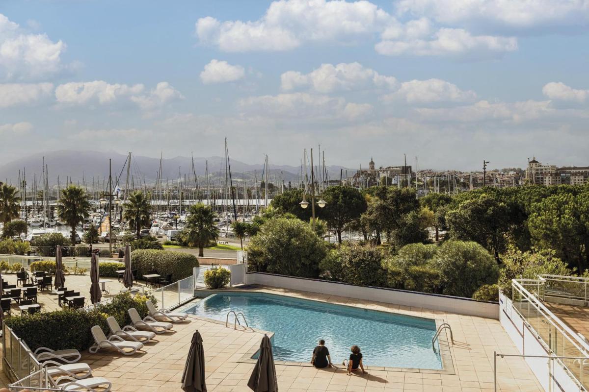 2 personnes assises dans une piscine avec vue sur le port dans l'établissement Hôtel Serge Blanco - Relais Thalasso & Spa, à Hendaye