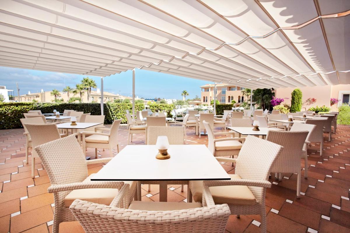 un patio con mesas, sillas y una sombrilla blanca en Grupotel Macarella Suites & Spa, en Son Xoriguer