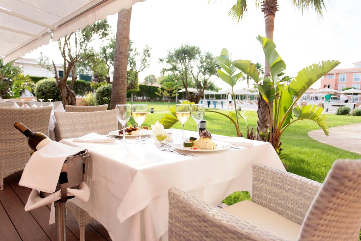 una mesa con copas de vino y comida en el patio en Grupotel Macarella Suites & Spa, en Son Xoriguer