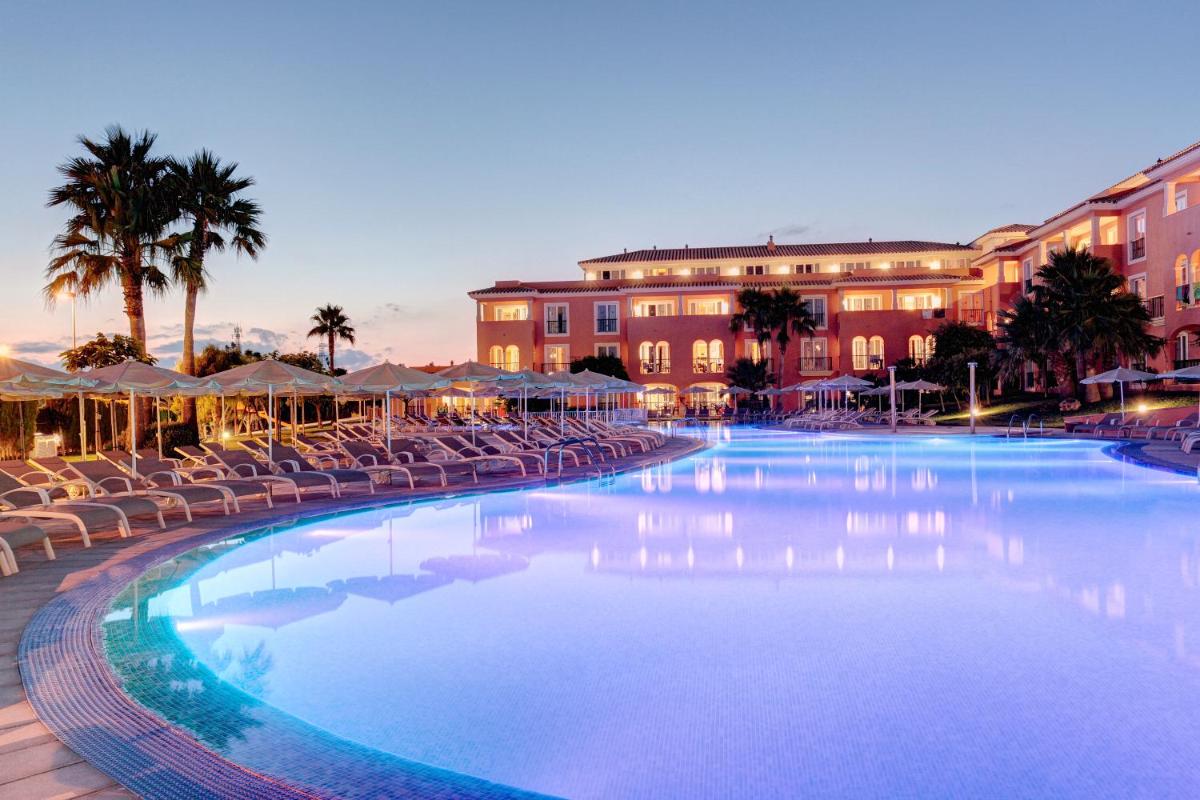 una gran piscina con sillas y edificios en Grupotel Macarella Suites & Spa, en Son Xoriguer