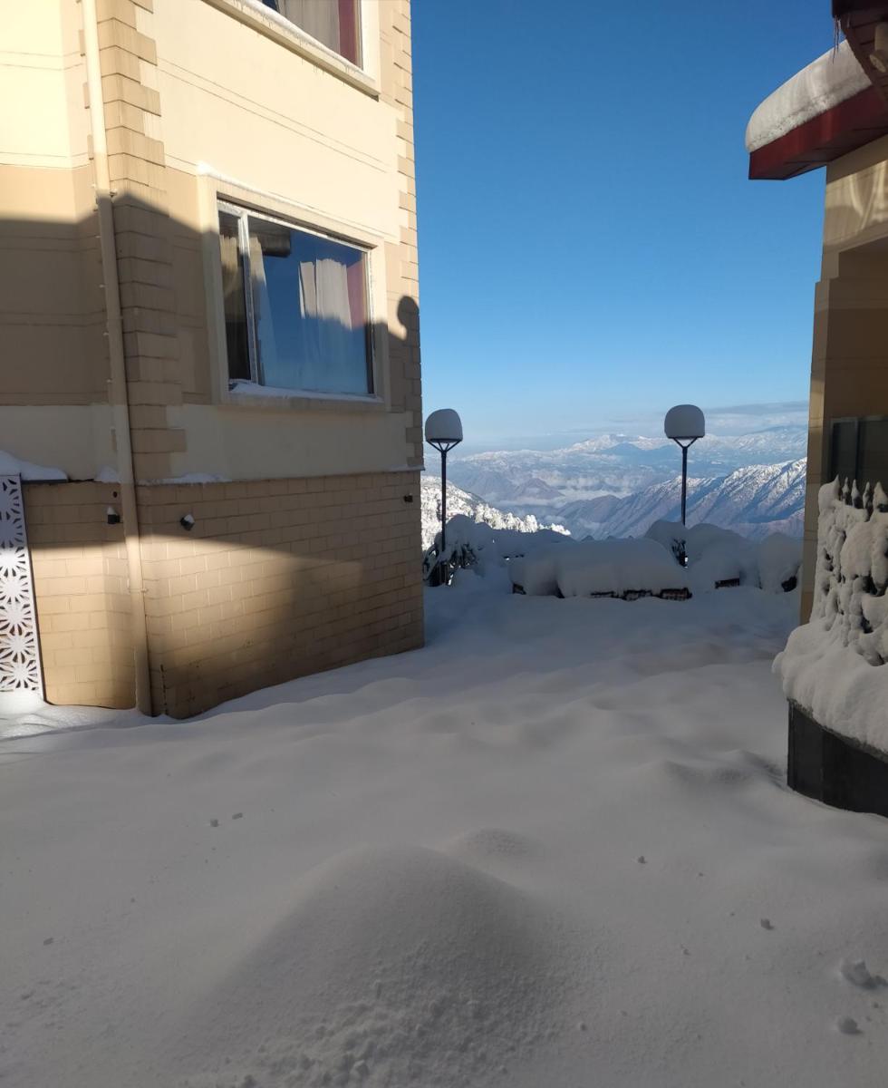 a snow covered yard with a building and mountains in the background at Radisson Kufri in Shimla