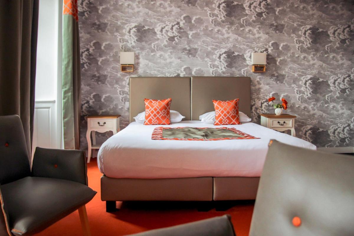 - une chambre avec un lit doté d'oreillers orange et d'une chaise dans l'établissement Hôtel Le Petit Périer, à Laval