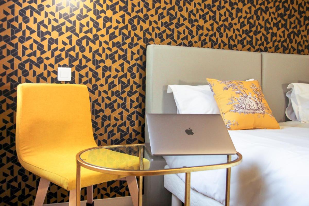 un ordinateur portable assis sur une chaise à côté d'un lit dans l'établissement Hôtel Le Petit Périer, à Laval