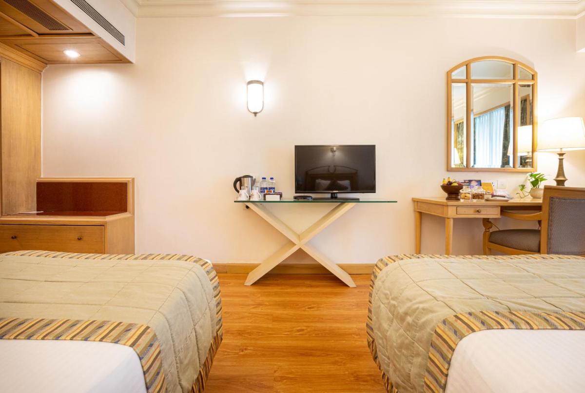 two beds in a room with a desk and a tv at The Orchid Hotel Mumbai Vile Parle in Mumbai