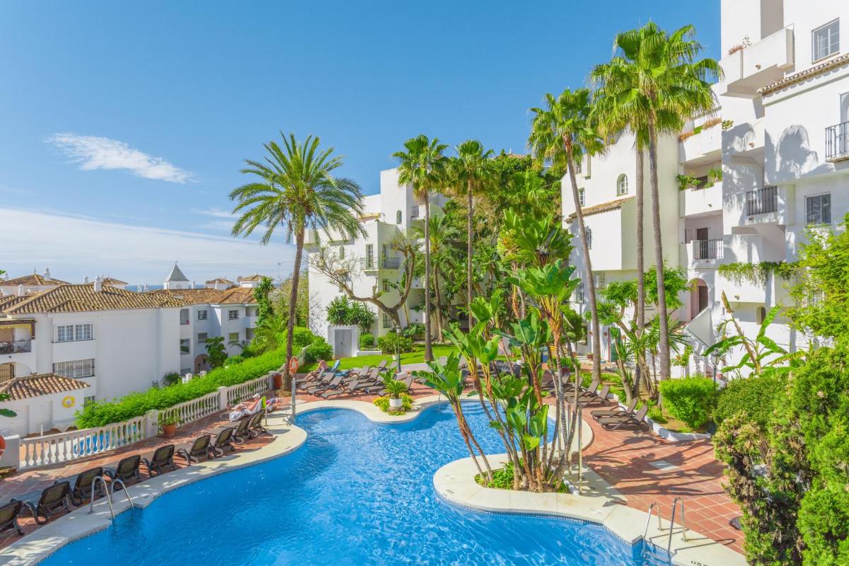 Una imagen de una piscina de un resort con sillas y palmeras. en Royal Oasis Club at Pueblo Quinta, en Benalmádena