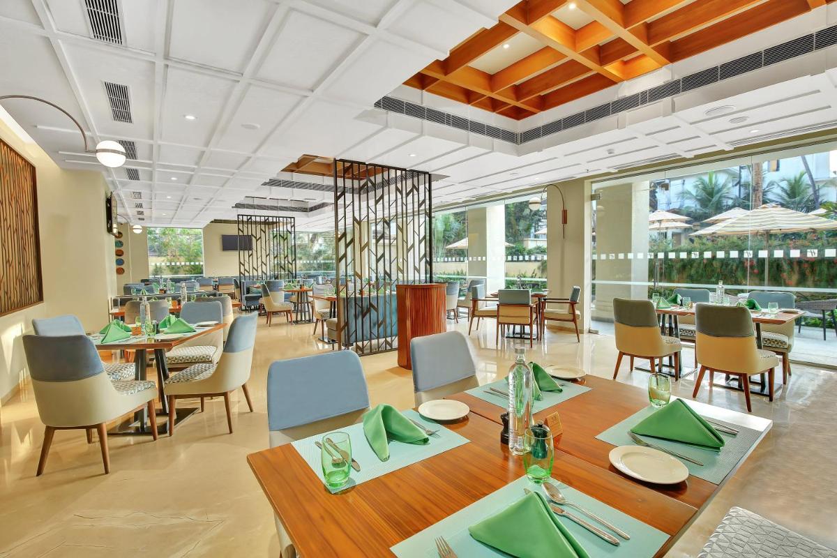a dining room with tables and chairs and windows at Holiday Inn Goa Candolim in Candolim a dining room with tables and chairs and windows at Holiday Inn Goa Candolim in Candolim