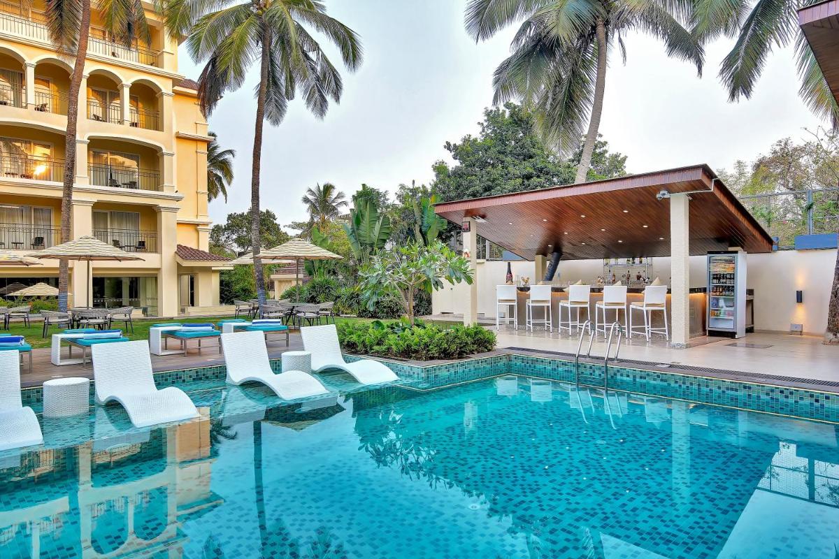 a swimming pool with white chairs and a building at Holiday Inn Goa Candolim in Candolim a swimming pool with white chairs and a building at Holiday Inn Goa Candolim in Candolim