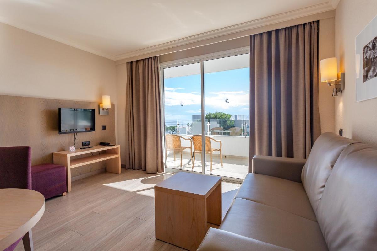 Una habitación de hotel con un sofá y vista a un balcón. en Marins Playa, en Cala Millor