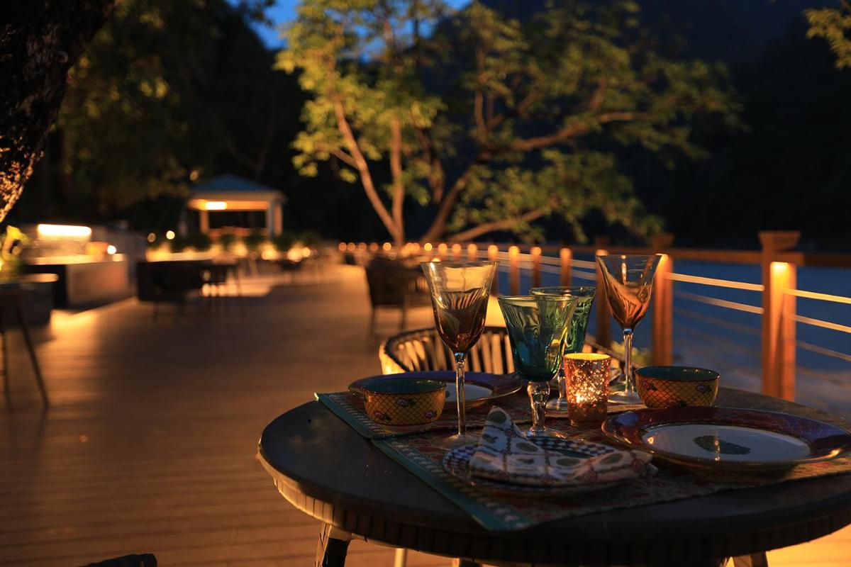 a table with plates and glasses on a deck at night at Anand Kashi by the Ganges Rishikesh - IHCL Seleqtions in Rishīkesh