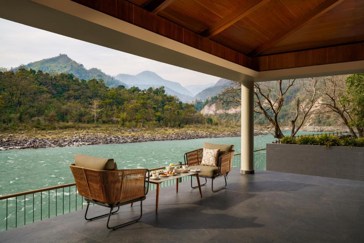 a porch with a table and chairs and a view of a river at Anand Kashi by the Ganges Rishikesh - IHCL Seleqtions in Rishīkesh