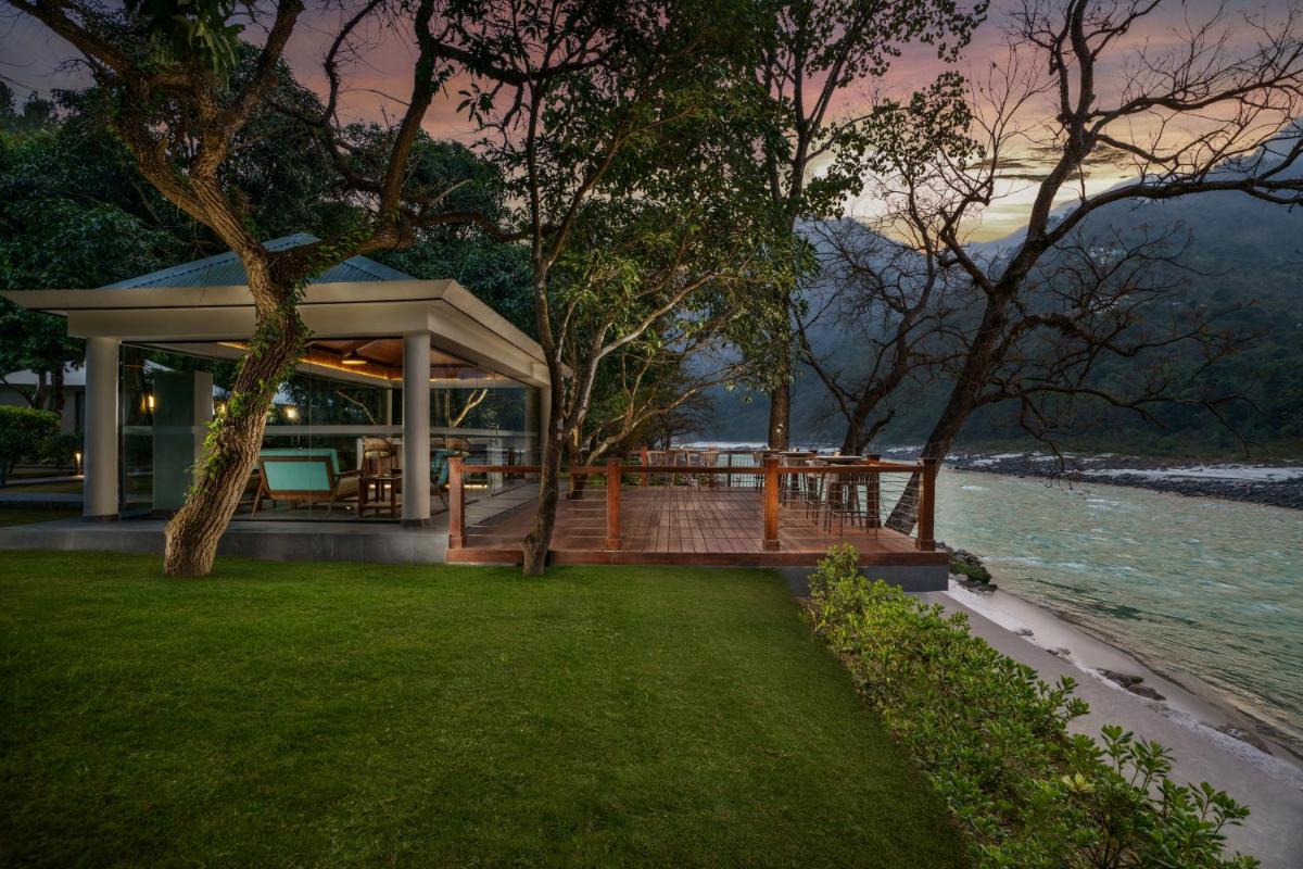 a house with a deck next to the water at Anand Kashi by the Ganges Rishikesh - IHCL Seleqtions in Rishīkesh