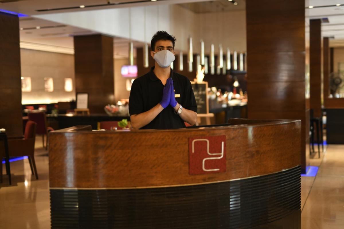 a man wearing a mask and a tie behind a counter at Radisson Blu Plaza Delhi Airport in New Delhi a man wearing a mask and a tie behind a counter at Radisson Blu Plaza Delhi Airport in New Delhi