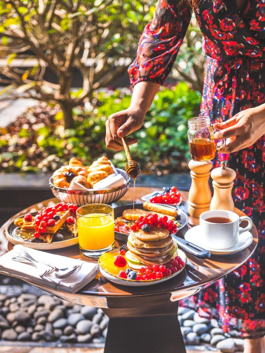a woman is preparing a breakfast table with pancakes and juice at Hyatt Regency Dehradun Resort and Spa in Dehradun