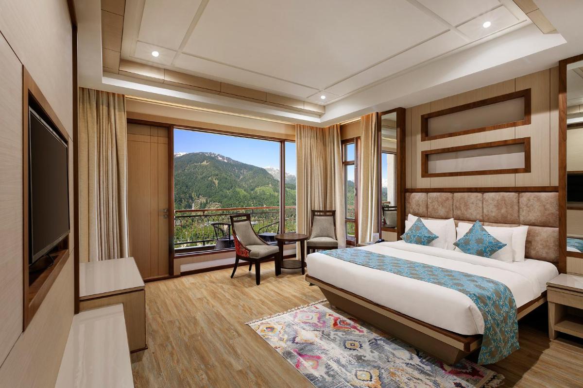 a hotel room with a bed and a large window at The Orchid Manali - a Boutique Hotel in Manāli a hotel room with a bed and a large window at The Orchid Manali - a Boutique Hotel in Manāli