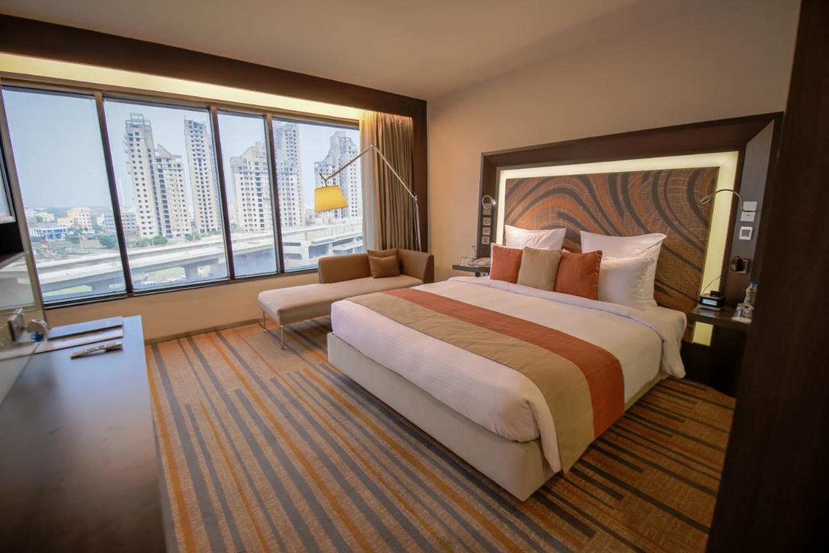 a hotel room with a large bed and large windows at Novotel Kolkata Hotel and Residences in Kolkata a hotel room with a large bed and large windows at Novotel Kolkata Hotel and Residences in Kolkata