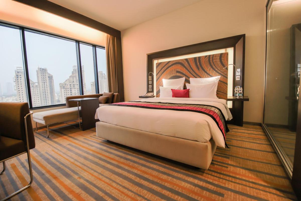 a hotel room with a large bed and large windows at Novotel Kolkata Hotel and Residences in Kolkata a hotel room with a large bed and large windows at Novotel Kolkata Hotel and Residences in Kolkata