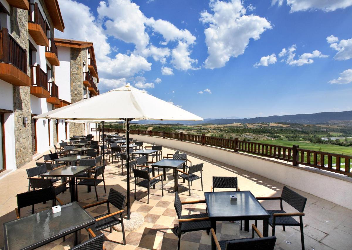 Un patio con mesas y sillas y una sombrilla. en Hotel & Spa Real Badaguás Jaca, en Badaguás